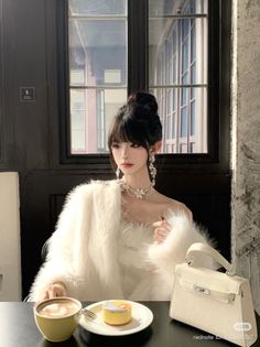Woman in a white fur coat with an updo, drinking coffee and eating dessert