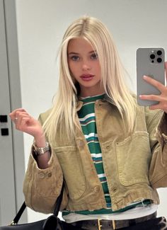 Blonde woman in a cropped jacket and striped shirt taking a mirror selfie