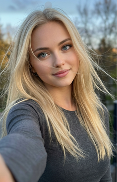 Blonde woman with blue eyes in a grey shirt taking a selfie outdoors