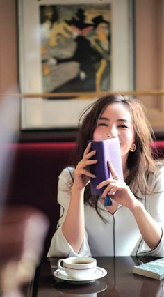 Woman with long hair holding a purple book, smiling in an indoor setting