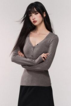 Woman with long black hair wearing a gray long-sleeve v-neck shirt with crossed arms