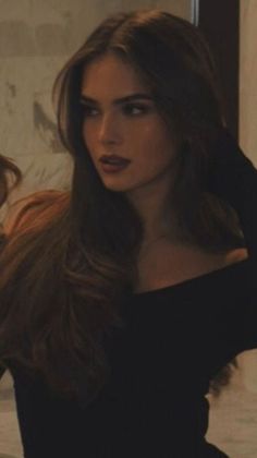 Woman with long dark hair and dark lipstick wearing an off-shoulder top indoors