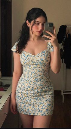 Woman in a floral dress taking a mirror selfie indoors