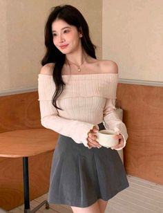 Woman in an off-shoulder top and pleated skirt holding a mug indoors