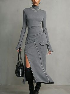 Woman in a gray dress with zipper details and black boots holding a handbag