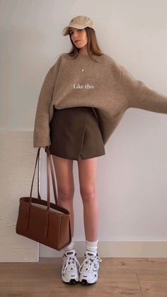 Woman in a baseball cap, oversized sweater, and mini skirt holding a tote bag