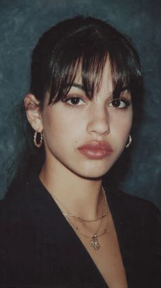 Woman with bangs and hoop earrings wearing layered necklaces and a black top