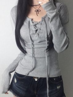 Person with long black hair wearing a gray long sleeve top and denim shorts