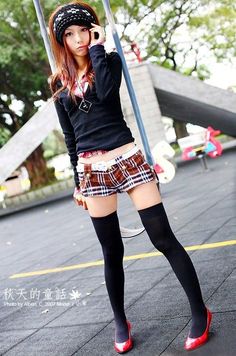 Woman in plaid shorts and thigh-high socks posing outdoors