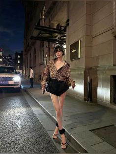 Woman in a leopard print shirt and black shorts on a city street at night