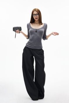 Woman with long hair and glasses wearing a gray top and wide leg pants