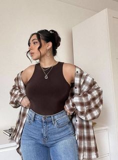 Woman in a brown top, plaid shirt, and blue jeans with an updo hairstyle
