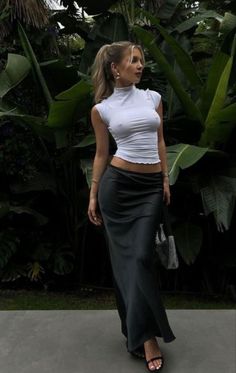 Woman in a white top and long skirt standing outdoors among tropical plants