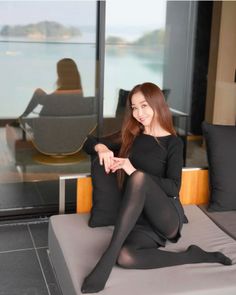 Woman in a black top and tights sitting on a couch indoors