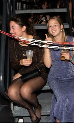 Two young women sitting on stairs at a party, holding drinks