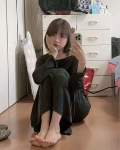 Woman with short hair taking a mirror selfie while sitting on the floor