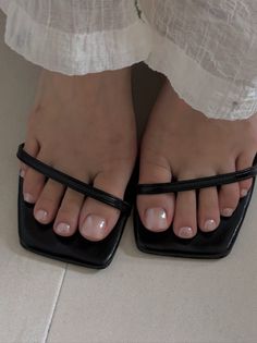 Feet in black sandals with a white dress and light pink pedicure