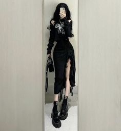 Person in a black outfit with a ruffled skirt and platform shoes taking a mirror selfie