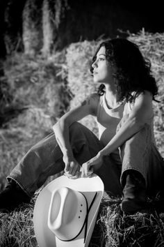 Woman with curly hair and a cowboy hat sitting on hay bales