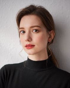 Woman in a black turtleneck with a ponytail and red lipstick looking at the camera