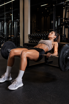 Woman performing hip thrusts with a barbell in a gym