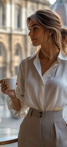 Woman in a white shirt and striped pants holding a coffee cup indoors