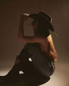 Woman in a cowboy hat and jeans, sitting with a cigarette, lit by backlight