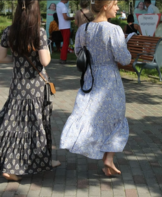 Two women in long dresses walking barefoot on a paved outdoor area