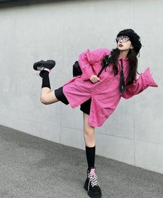 Person in a pink shirt, black shorts, and beret posing outdoors