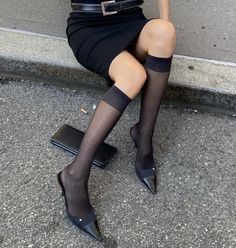 Person in a black skirt and knee-high socks sitting on a curb