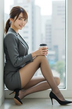Woman in a gray business suit and pantyhose holding a coffee cup by a window