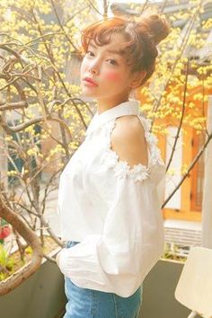 Woman in a white blouse with exposed shoulders and jeans outdoors with yellow flowers