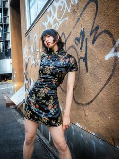 Woman in a black cheongsam dress posing against a graffiti wall