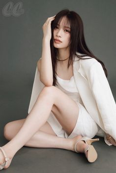 Woman with long dark hair in a white outfit and high heels sitting on the floor
