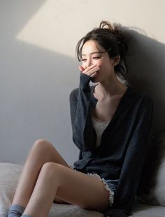 Woman with a messy bun covering her mouth, sitting indoors with soft lighting