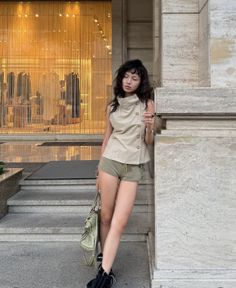 Woman in a sleeveless top and short shorts leaning against a building