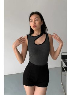 Woman with dark hair wearing a gray cutout top and black shorts indoors