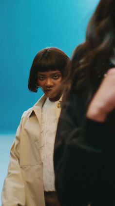 Person with short hair making a funny face, wearing a trench coat and sweater