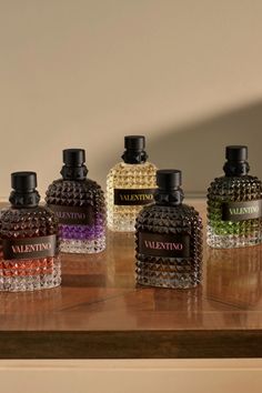 Six Valentino perfume bottles with colorful liquids on a wooden surface