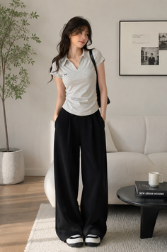 Woman in a grey polo shirt and black wide leg pants standing indoors