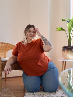 Woman with blonde hair and a tattoo kneeling indoors, smiling at the camera