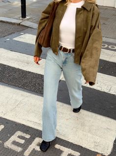 Person in a suede jacket and light wash jeans walking on a crosswalk