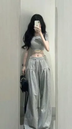 Woman with long black hair taking a mirror selfie in a crop top and wide leg pants