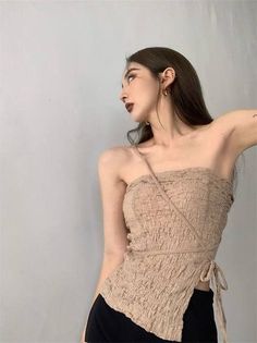 Woman with long hair wearing a beige strapless top and black pants indoors