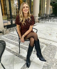 Woman in a leopard print dress and black boots sitting outdoors