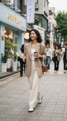 Woman in a blazer and wide-leg pants walking on a city street with a coffee cup