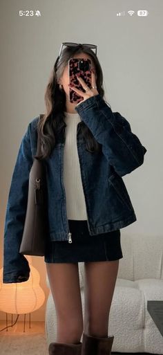 Woman in a denim jacket and mini skirt taking a mirror selfie