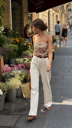 Woman in a strapless top and white pants walking past a flower shop