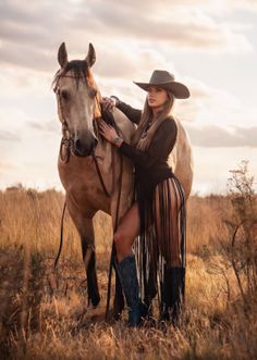 Woman in a cowboy hat and fringed outfit posing with a horse at golden hour