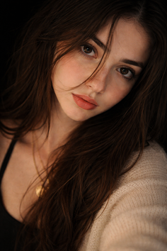 Woman with long brown hair and a gold necklace against a dark background